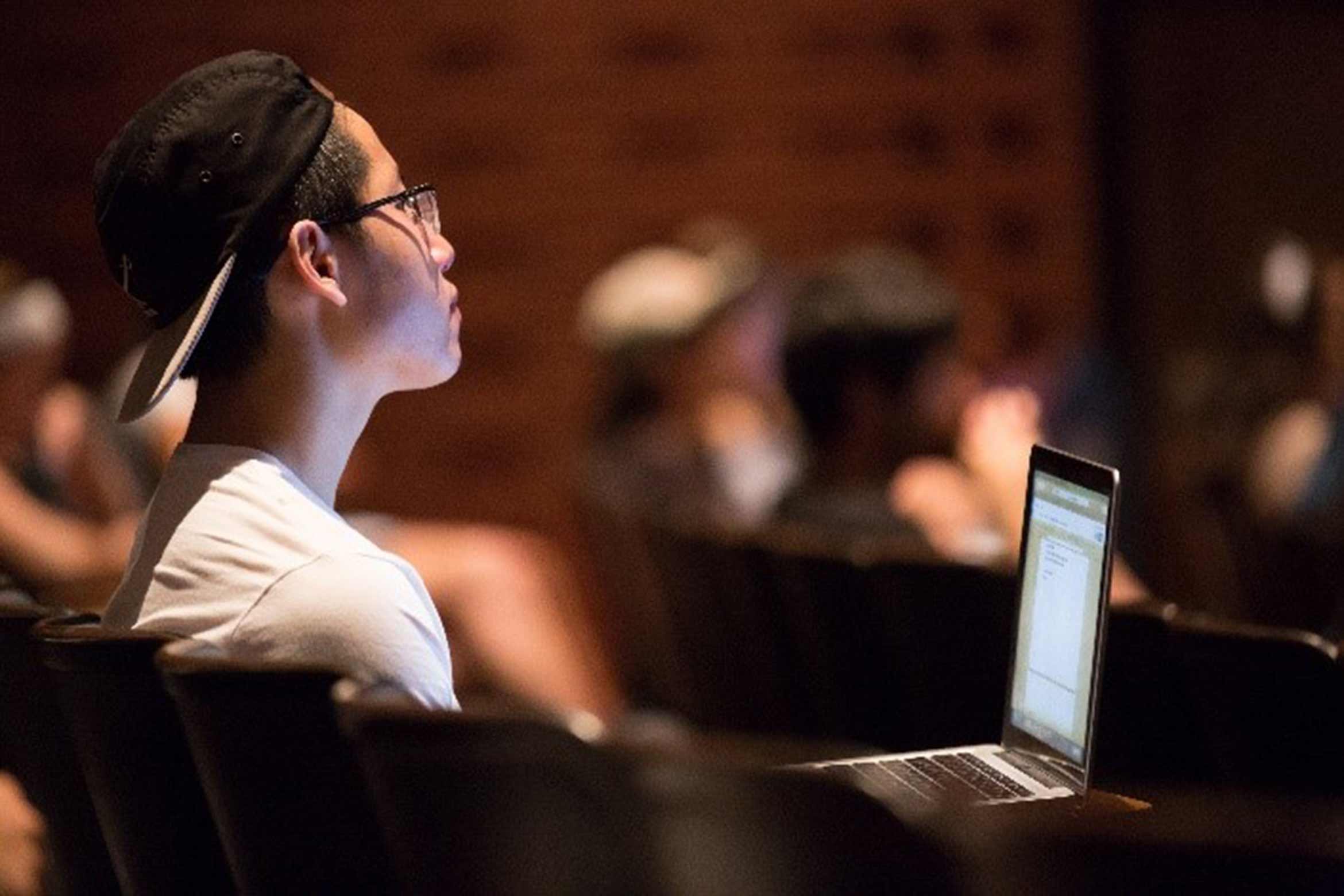 A student in class illuminated by their laptop screen.