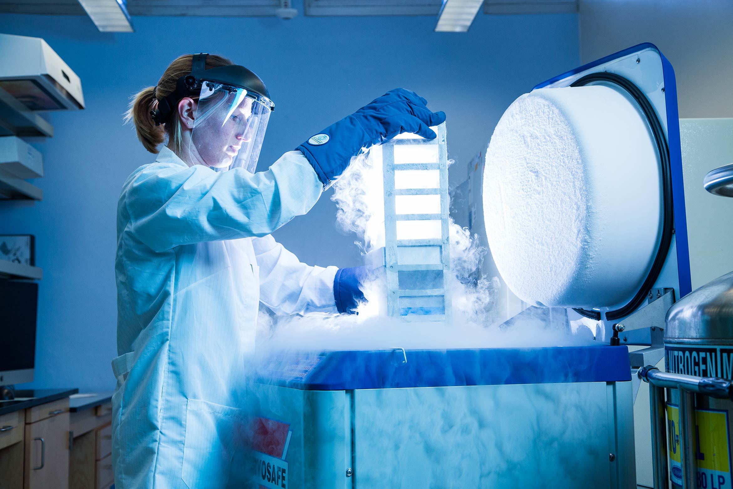 A researcher removing samples from a liquid nitrogen tank overflowing with a white fog of condensed cold air.