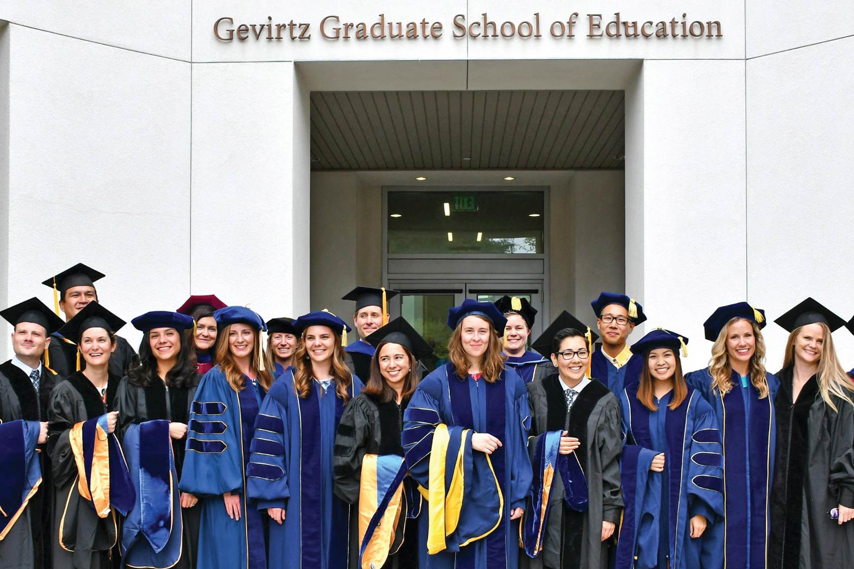 GGSE graduates in regalia stand in front of the GGSE building after graduation.
